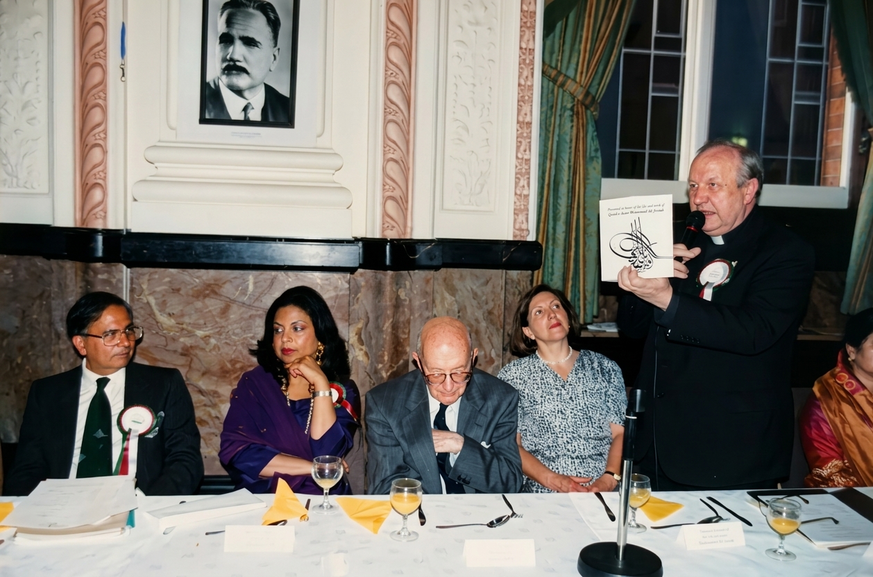 Guests at an Academy dinner, with a framed portrait of Iqbal on the wall and a speaker presenting a commemorative booklet.